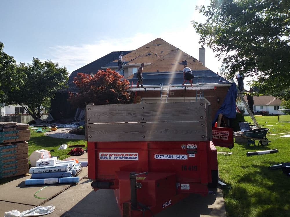 Roofing project in progress on a home, with workers installing new shingles and a dumpster nearby.
