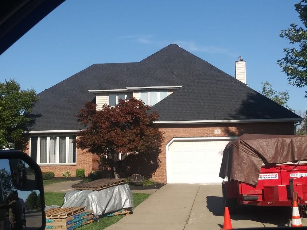 Two-story brick house with a steep roof, garage, and landscaping, under clear blue skies.