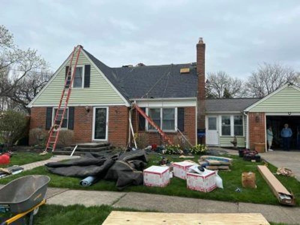 Roof renovation project on a brick house with ladders and landscaping work in progress.