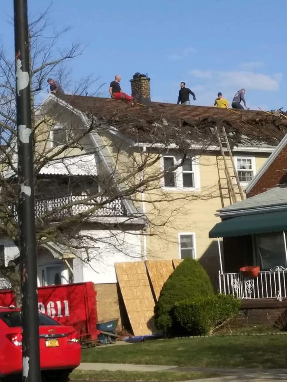 Roof repair crew working on a home, removing shingles under a clear blue sky.