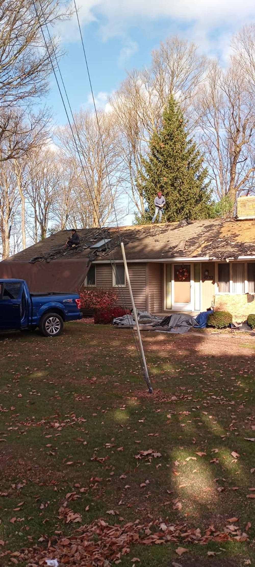 Roof repair in progress on a residential home with workers and a blue truck in the yard.